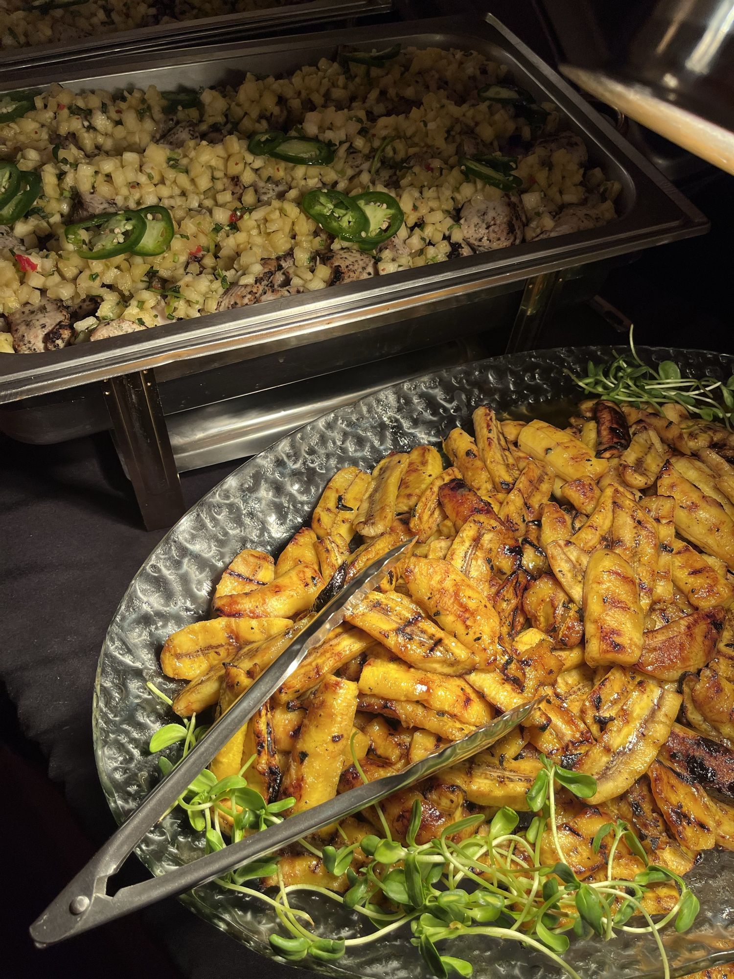 Grilled plantain and a chafing dish of seasoned chicken on a Chef Chelsae Marie catering line
