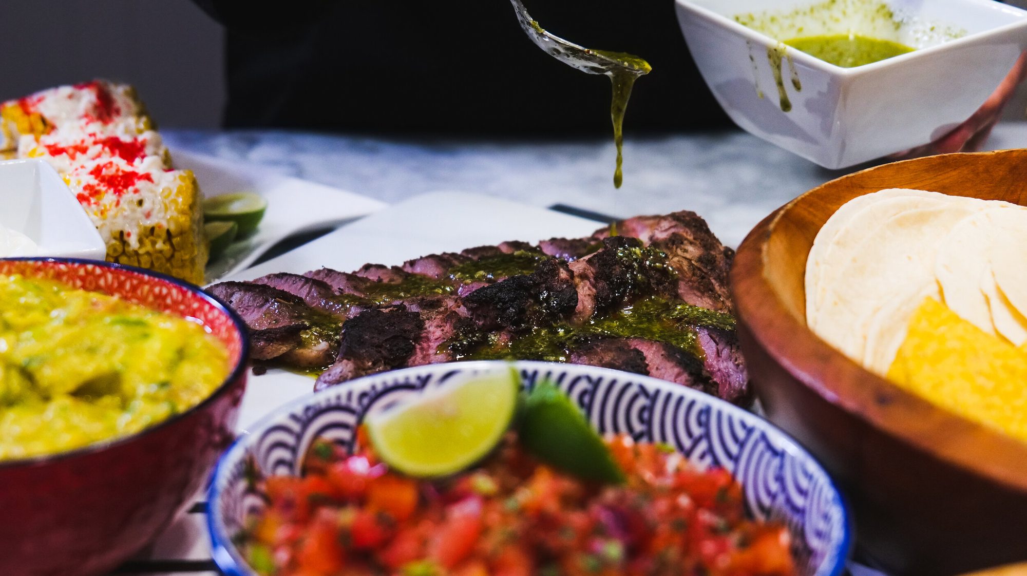 Guests reaching for curry, grilled meats and salsas on a shared Chef Chelsae Marie table