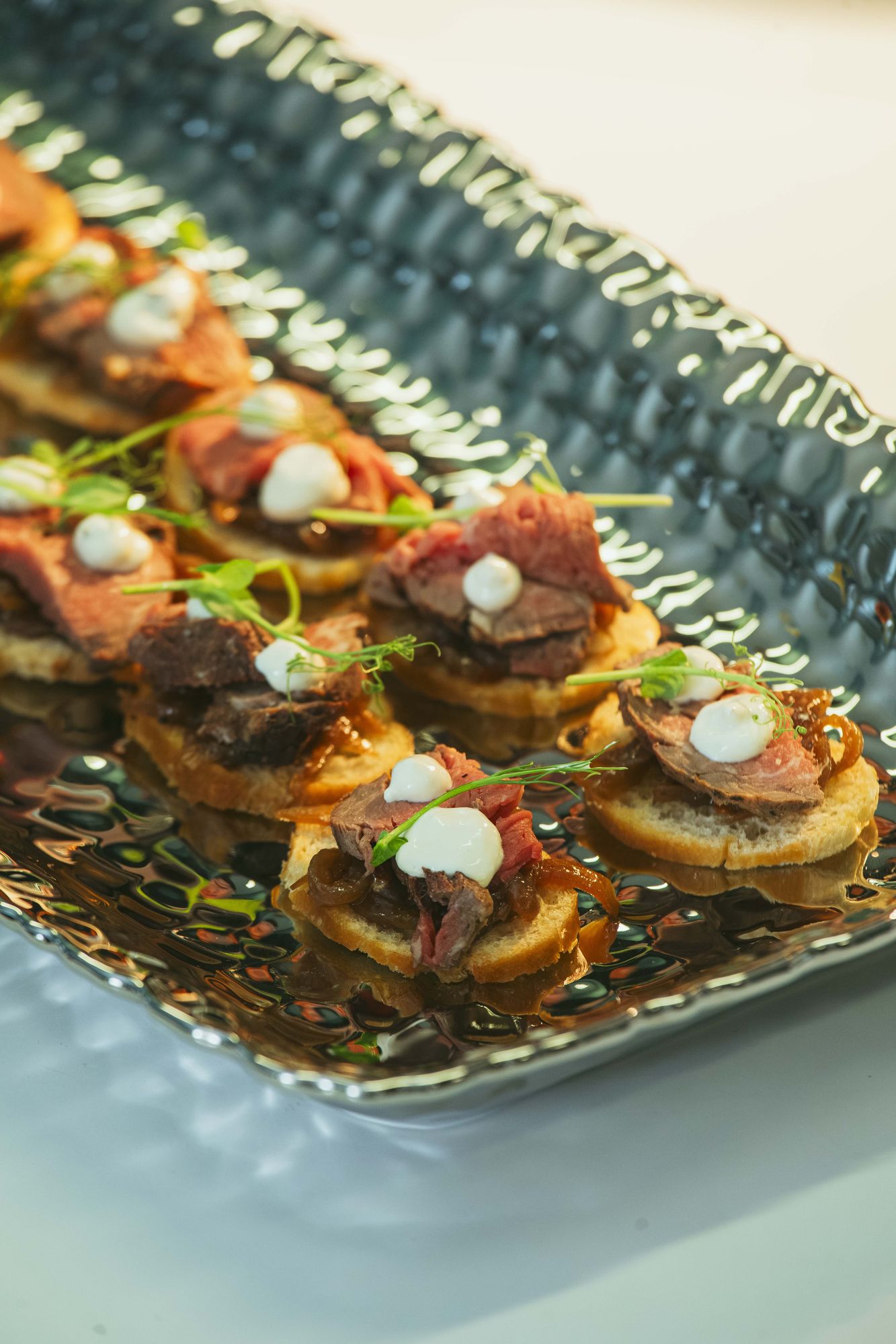 Plantain canapés topped with seared beef and cream on a long blue platter
